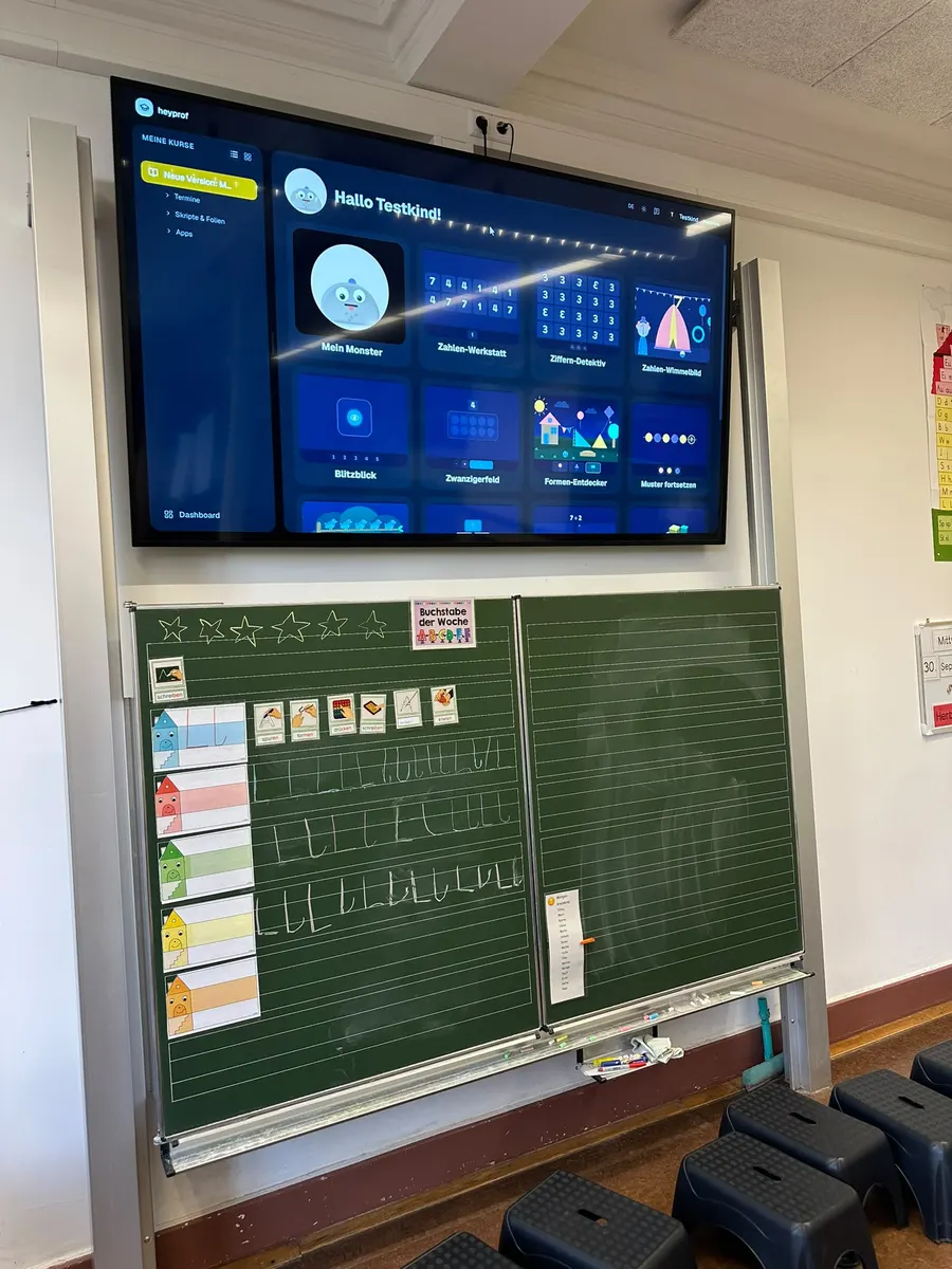 Klassenzimmer: großer Bildschirm über der Tafel zeigt die heyprof-Kinderansicht mit den Mathe-Apps